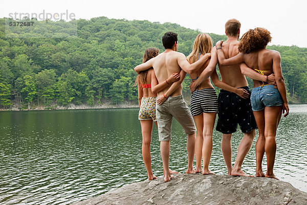Freunde stehen zusammen auf einem Felsen am Seeufer.