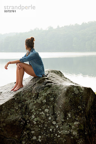 Junge Frau sitzend auf einem Felsen mit Blick auf See