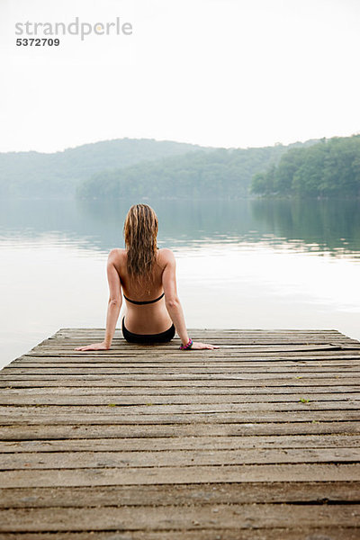 Junge Frau am Pier sitzend mit Blick auf den See