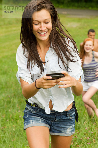 Teenage Girl looking at Handy während des Gehens in Landschaft mit Freunden