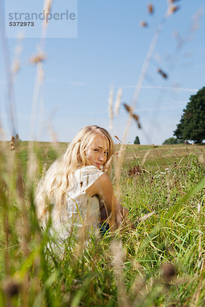 Young Woman sitting in einem Feld  rückwärts Lächeln in die Kamera