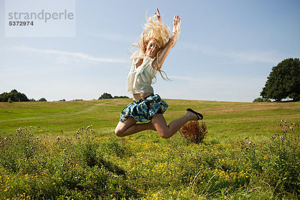 Junge Frau auf einem Feld  die in die Luft springt.
