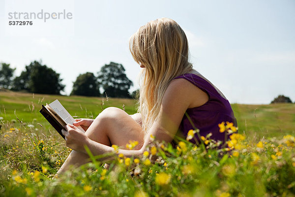 Junge Frau beim Lesen eines Buches auf einem Feld