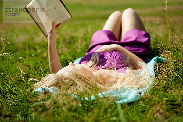 Young Woman lying down ein Buch in einem Feld zu lesen