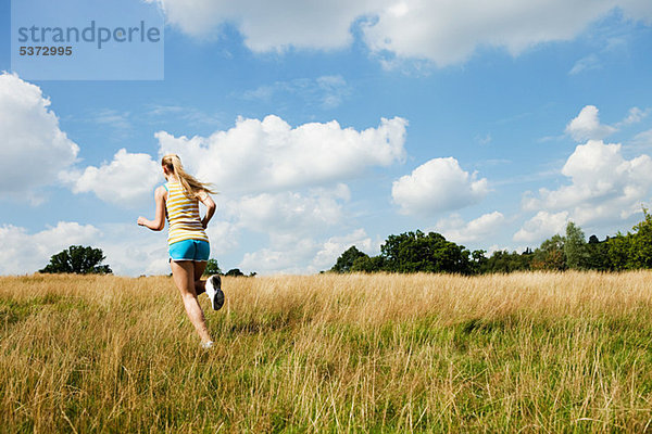 Junge Frau beim Joggen durch ein Feld an einem sonnigen Tag