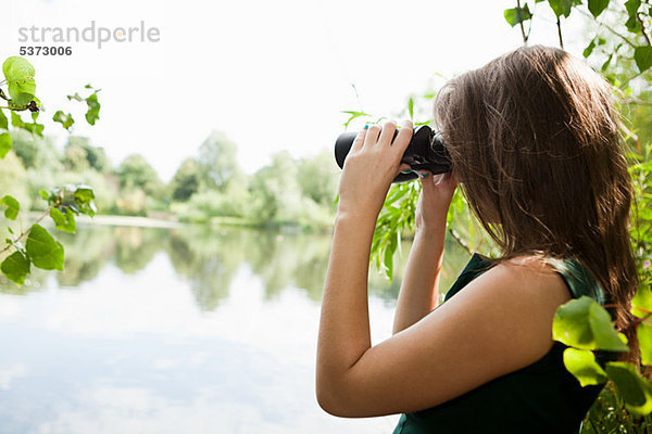 Junge Frau  die durch ein Fernglas über einen See schaut