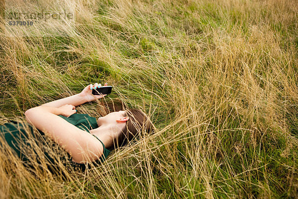 Junge Frau liegen in einem Feld mit ihrem Handy