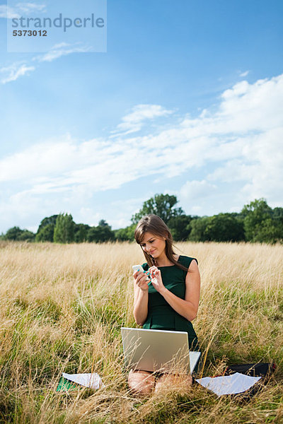 Junge Frau mit Laptop und Handy mitten in einem Feld