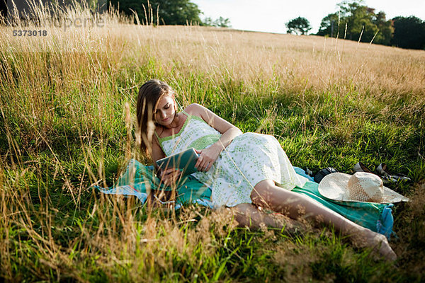 Junge Frau liegen auf Seite in einem Feld auf ein Handgerät