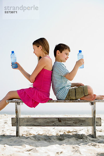 Mädchen und Junge mit Wasserflaschen am Strand