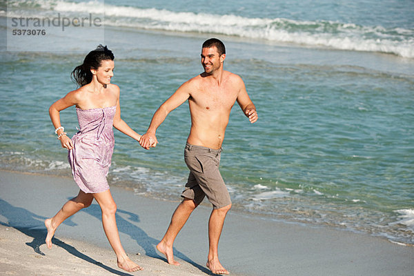Junges Paar  die entlang den Rand des Wassers am Strand