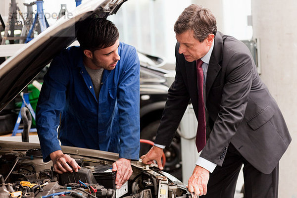 Geschäftsmann beim Blick auf den Automotor mit Mechaniker