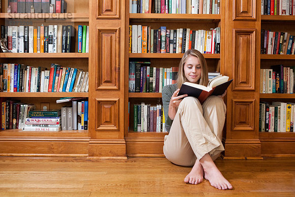 Junge Frau liest auf dem Boden bei den Bücherregalen
