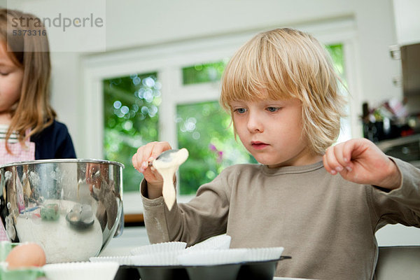 Junge löffelt Kuchen Mischung in Kuchen Fällen