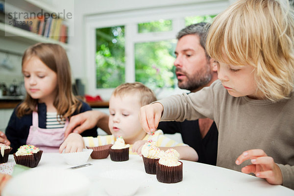 Mittlerer Erwachsener Mann und Familie dekorieren Cupcakes