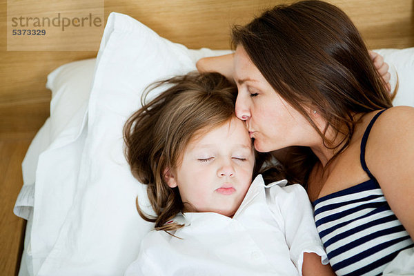 Mittlere erwachsene Frau küsst schlafende Tochter