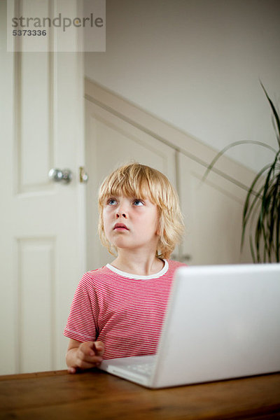 Boy looking up von Laptop auf Schreibtisch