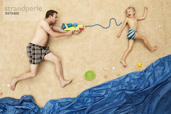 Deutschland  Vater und Sohn spielen mit Wasserpistolen am Strand