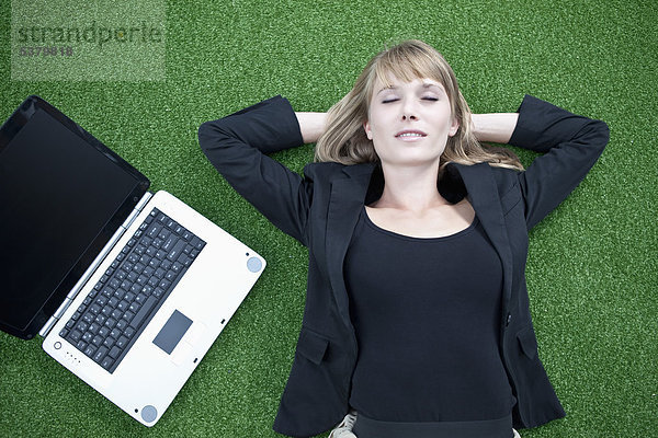 Geschäftsfrau entspannt auf dem Rasen neben dem Laptop
