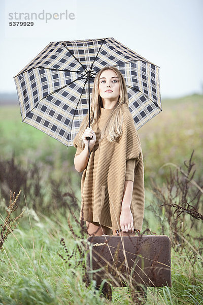 Junge Frau mit Regenschirm und Aktentasche aus Gras