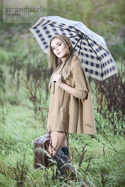 Junge Frau mit Regenschirm und Aktentasche aus Gras