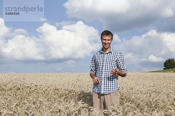 Mann im Weizenfeld stehend  lächelnd  Portrait