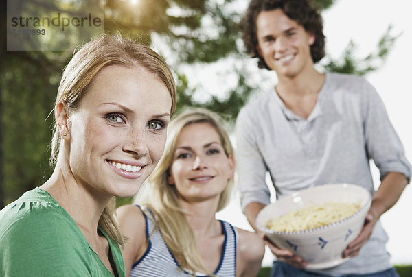 Italien  Toskana  Magliano  Junger Mann hält Schale mit Pasta und Frauen im Vordergrund  lächelnd  Portrait