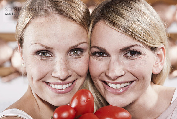 Italien  Toskana  Magliano  Nahaufnahme von zwei jungen Frauen mit Tomaten in der Küche  lächelnd  Portrait