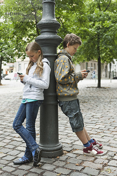 Junge und Mädchen  die sich auf Poller mit Handy stützen