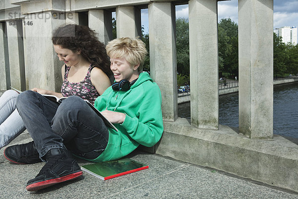 Deutschland  Berlin  Teenagerpaar auf Brücke sitzend und lesend