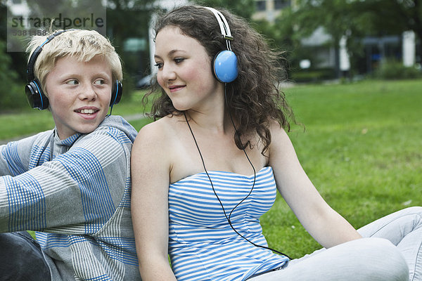 Deutschland  Berlin  Teenagerpaar mit Kopfhörer beim Musikhören im Park