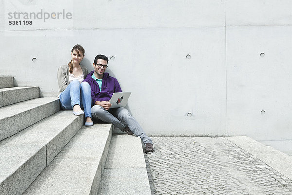 Deutschland  Berlin  Paar mit Laptop im Treppenhaus