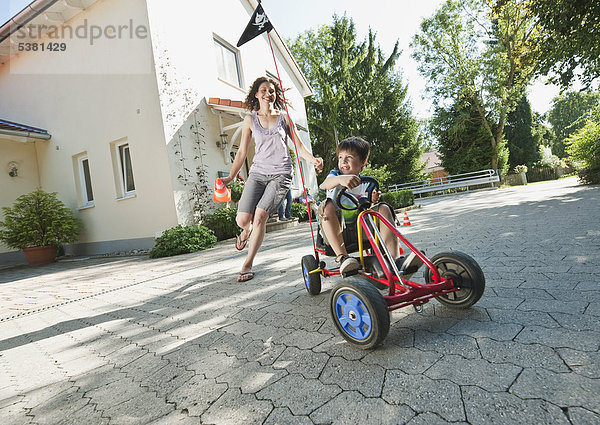 Junge mit Fahrpedal Go-Kart und Frau mit Familie im Hintergrund