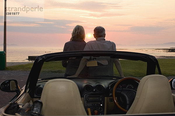 Paar bewundert Sonnenuntergang im Cabriolet