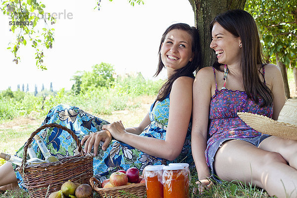 Lächelnde Frauen picknicken im Obstgarten