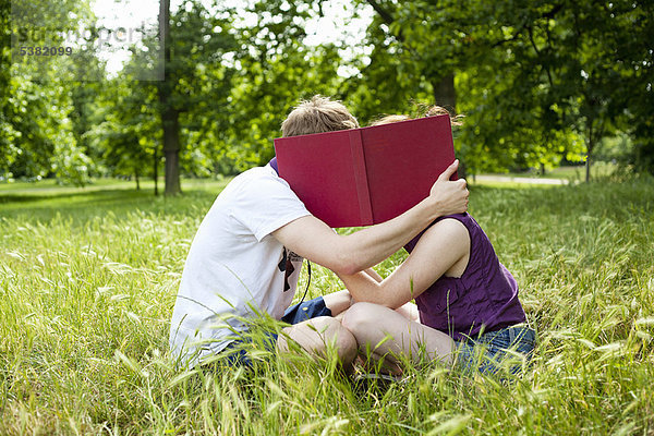 Teenager verstecken sich hinter einem Buch im Park