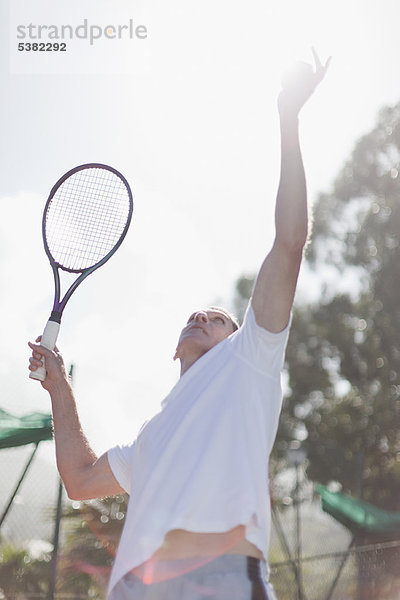 Älterer Mann serviert Tennisball