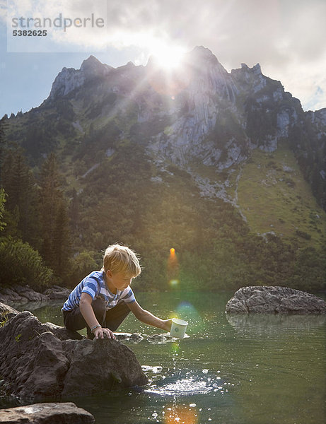 Junge taucht Becher in den stillen See