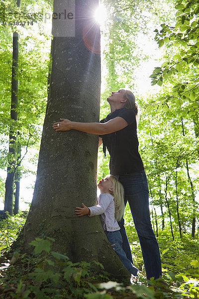Mutter und Tochter umarmen Baum