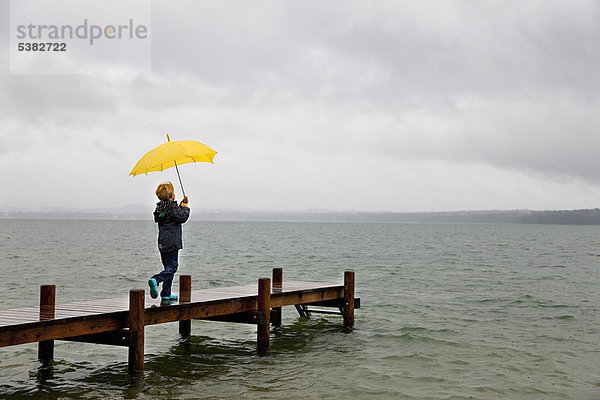 Junge mit Regenschirm auf Holzdock