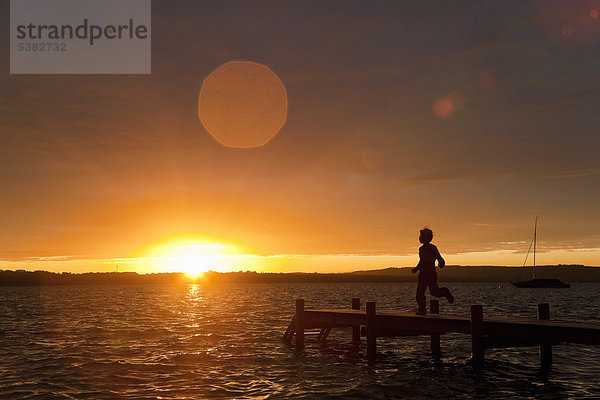 Junge rennt bei Sonnenuntergang auf Holzdock