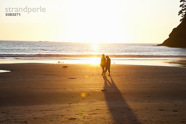 Paar Spaziergänge am Strand bei Sonnenuntergang
