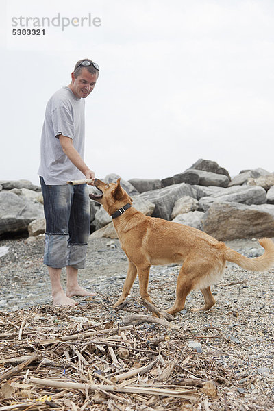 Mann spielt mit Hund am felsigen Strand