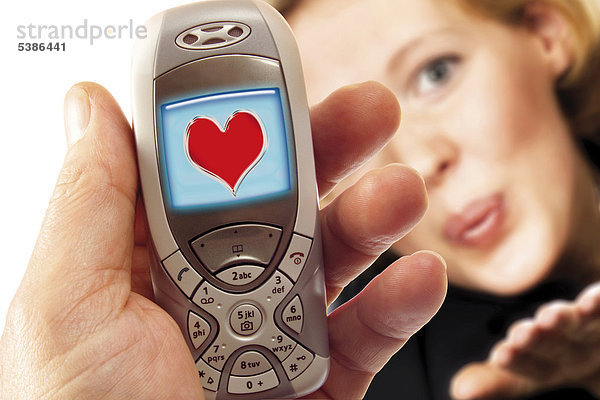 Hand hält Handy mit Herzlogo  im Hintergrund eine junge Frau - Symbol für Liebes-SMS