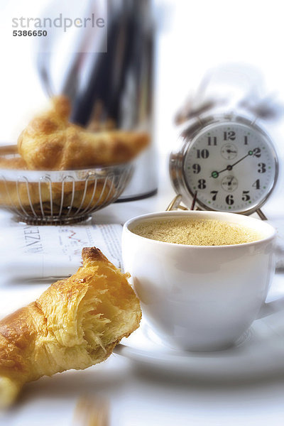 Frühstücksszene: Croissants  Kaffeetasse  Kaffeekanne  Zeitung und Wecker