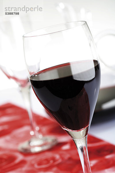 Rotweingläser auf Tischläufer mit Weinkaraffe iim Hintergrund