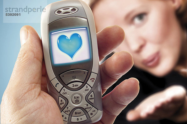Handy mit blauem Herz  im Hintergrund junge Frau - Symbol für Liebesgruß