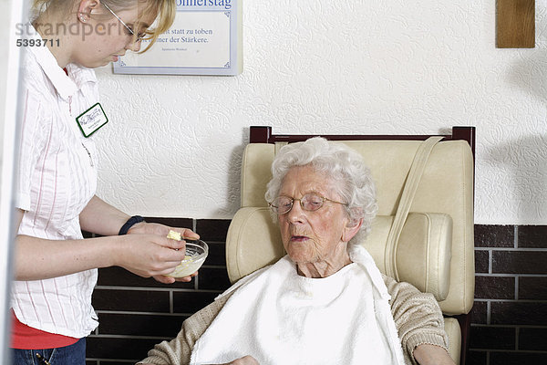 Im Pflegeheim  Altenheim  Pflegerin reicht einer Seniorin Essen an