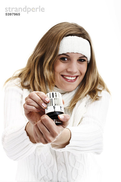 Junge Frau im weißen Rollkragenpullover mit Stirnband hält Heizungsthermostat