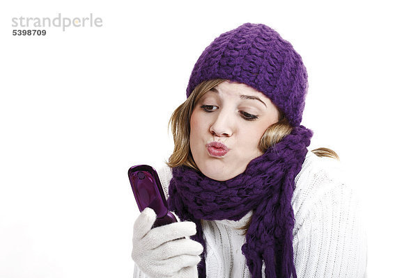 Junge Frau mit lila Wollmütze und Schal mit Handy mund